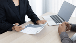 two business people sitting at a table with papers and a laptop