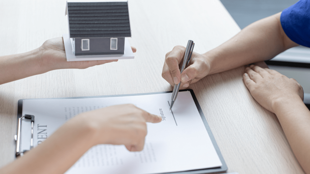 two people signing a document with a house model on top of it