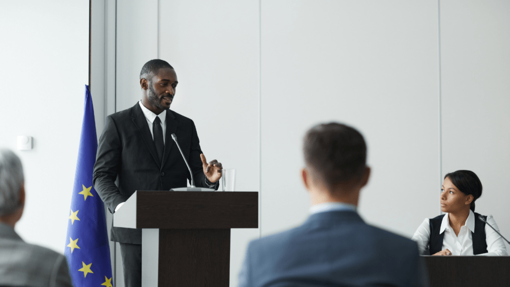 a person in a suit is giving a speech in front of a group of people