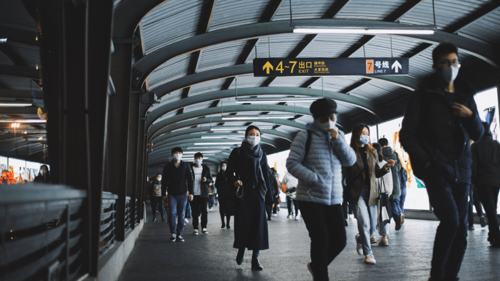 people wearing face masks walk through a subway station