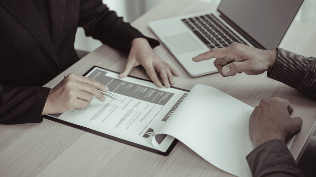 two business people sitting at a table with papers and a laptop