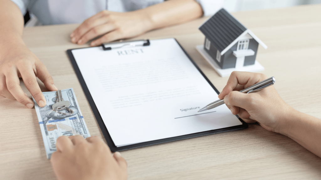 two people signing a document with a house model on top of it